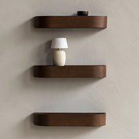 Dark wood shelves with smooth, curved edges against a light, textured wall featuring a minimalist lamp.