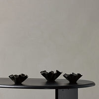 Set of three black ceramic bowls with wavy edges on a dark wooden table against a soft, neutral background.