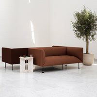 Stylish brown sofa with minimalist design, paired with a white side table and greenery. Modern elegance in a serene setting.