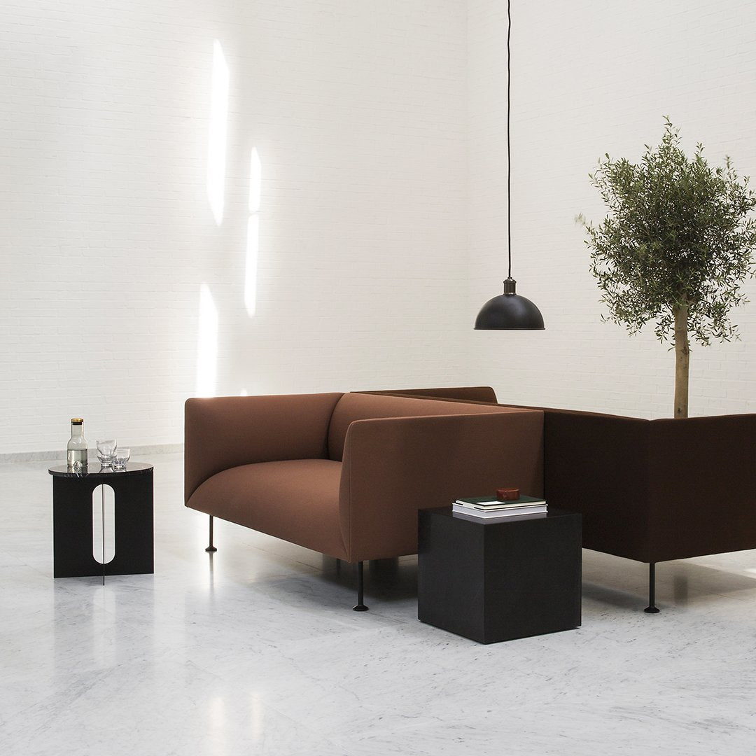 Brown minimalist sofa with a sleek black side table and green plant, set against a light-toned wall. Modern decor.