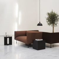 Brown minimalist sofa with a sleek black side table and green plant, set against a light-toned wall. Modern decor.