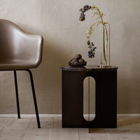 Black accent table with a modern design, featuring smooth surfaces and a circular cutout, paired with a neutral backdrop.