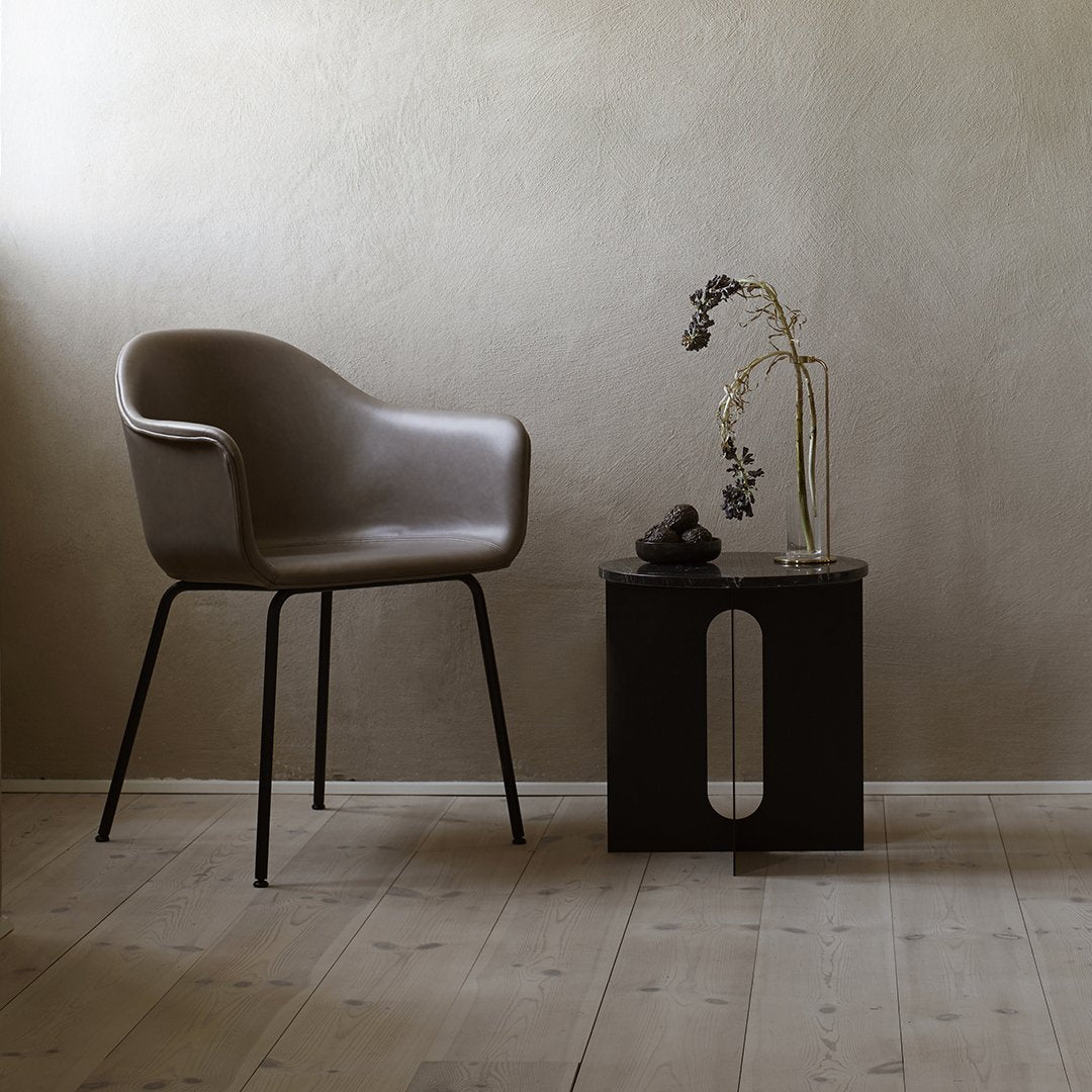 Light brown armchair with sleek black legs, paired with a dark wood side table. Minimalist design in neutral tones.