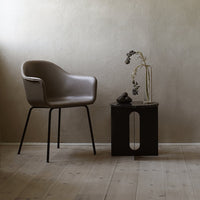 Light brown armchair with sleek black legs, paired with a dark wood side table. Minimalist design in neutral tones.