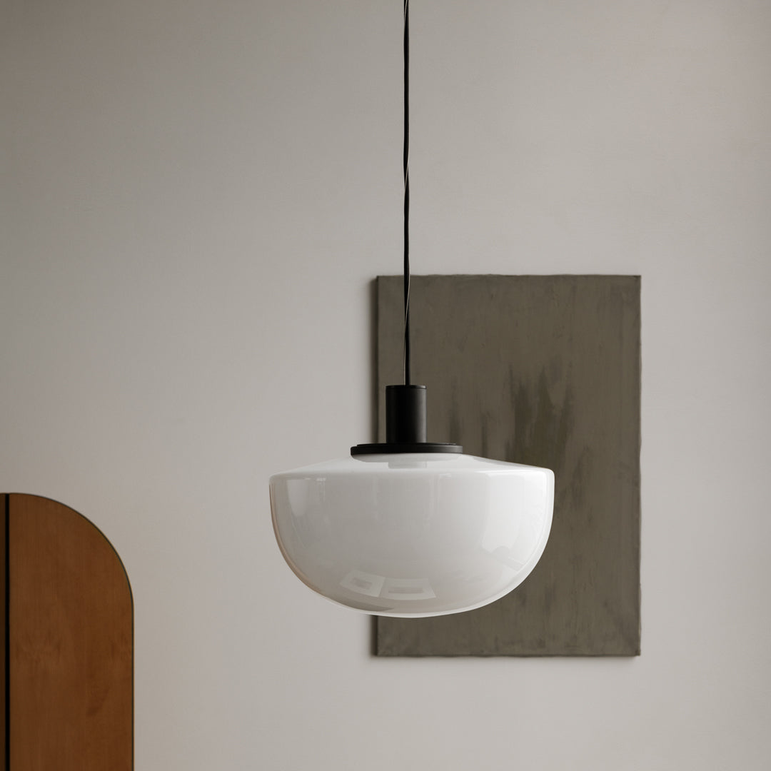 Glossy white pendant light with a smooth, curved shape and black accent, against a neutral wall and soft, muted backdrop.