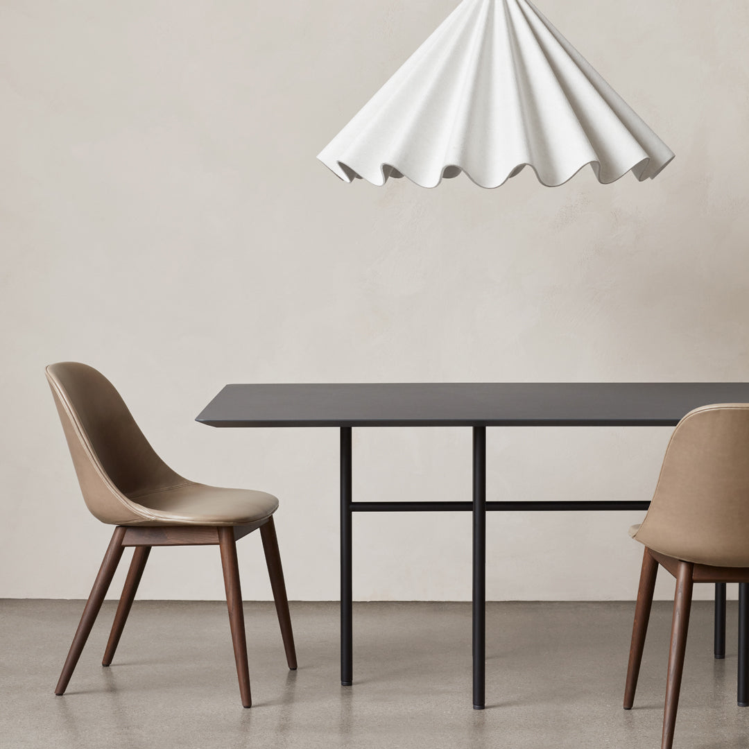 Minimalist brown and beige chairs beside a sleek black table under a white, scalloped pendant lamp.