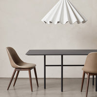 Minimalist brown and beige chairs beside a sleek black table under a white, scalloped pendant lamp.