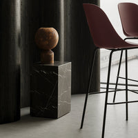 Black marble side table with white veins, contrasting warm wood accent, and dark red bar stools in a modern setting.