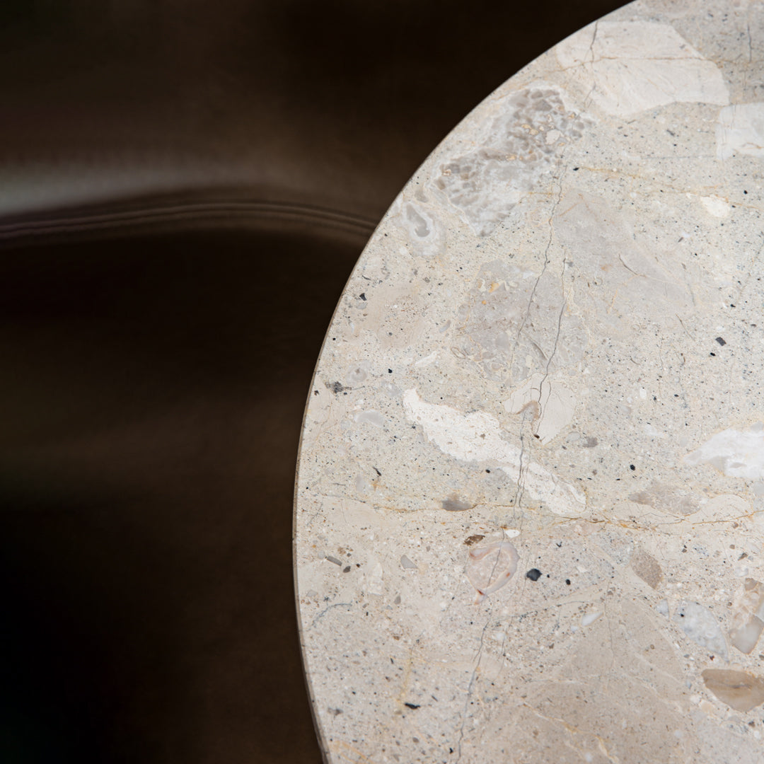Round beige stone table with subtle patterns and speckles against a dark background. Ideal for modern decor.