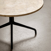 Round table with a beige marble top and sleek black metal legs, showcasing a modern and minimalist design.
