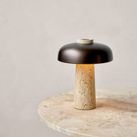 Modern lamp featuring a dark bronze shade and a textured beige stone base on a marble surface.