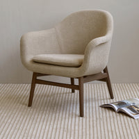 Beige upholstered accent chair with warm brown wooden legs, set on a textured cream striped rug.