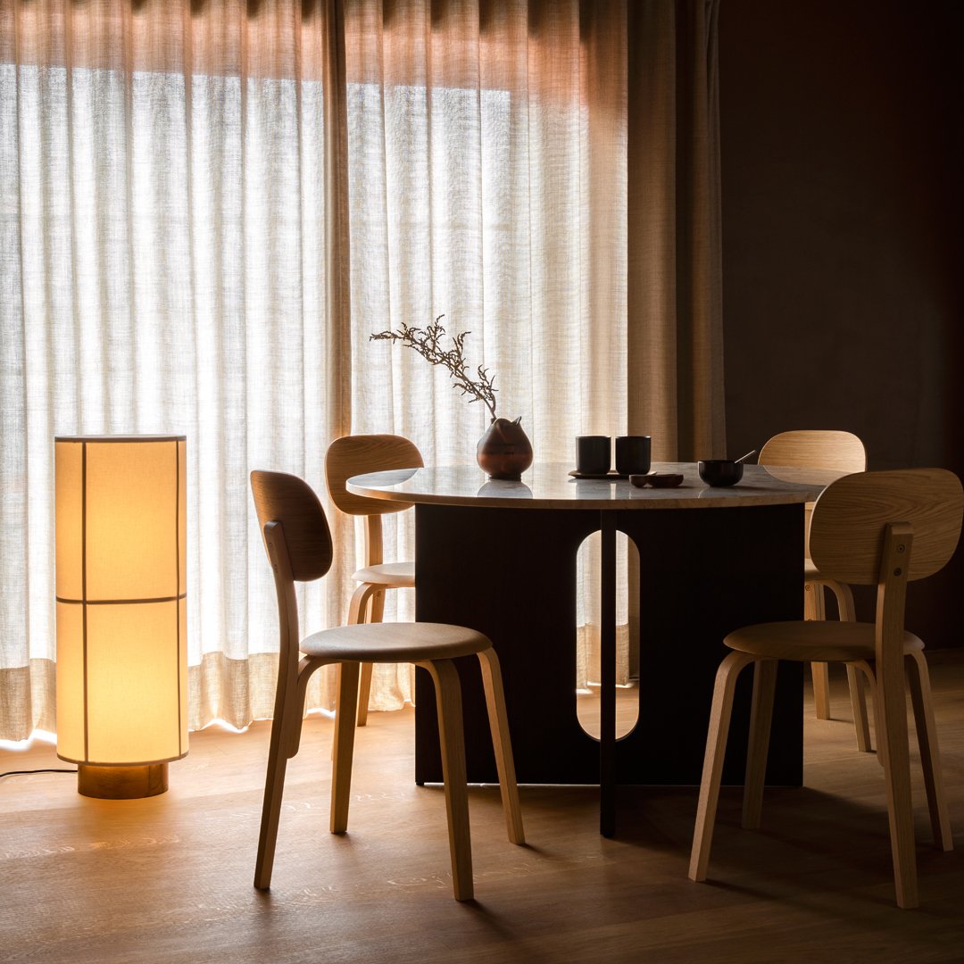 Modern dining table with a sleek black finish and light wood chairs, complemented by soft beige curtains and warm lighting.