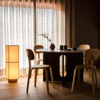 Modern dining table with a sleek black finish and light wood chairs, complemented by soft beige curtains and warm lighting.