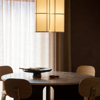 Modern round dining table in warm wood tones, surrounded by beige chairs, with soft light filtering through sheer curtains.