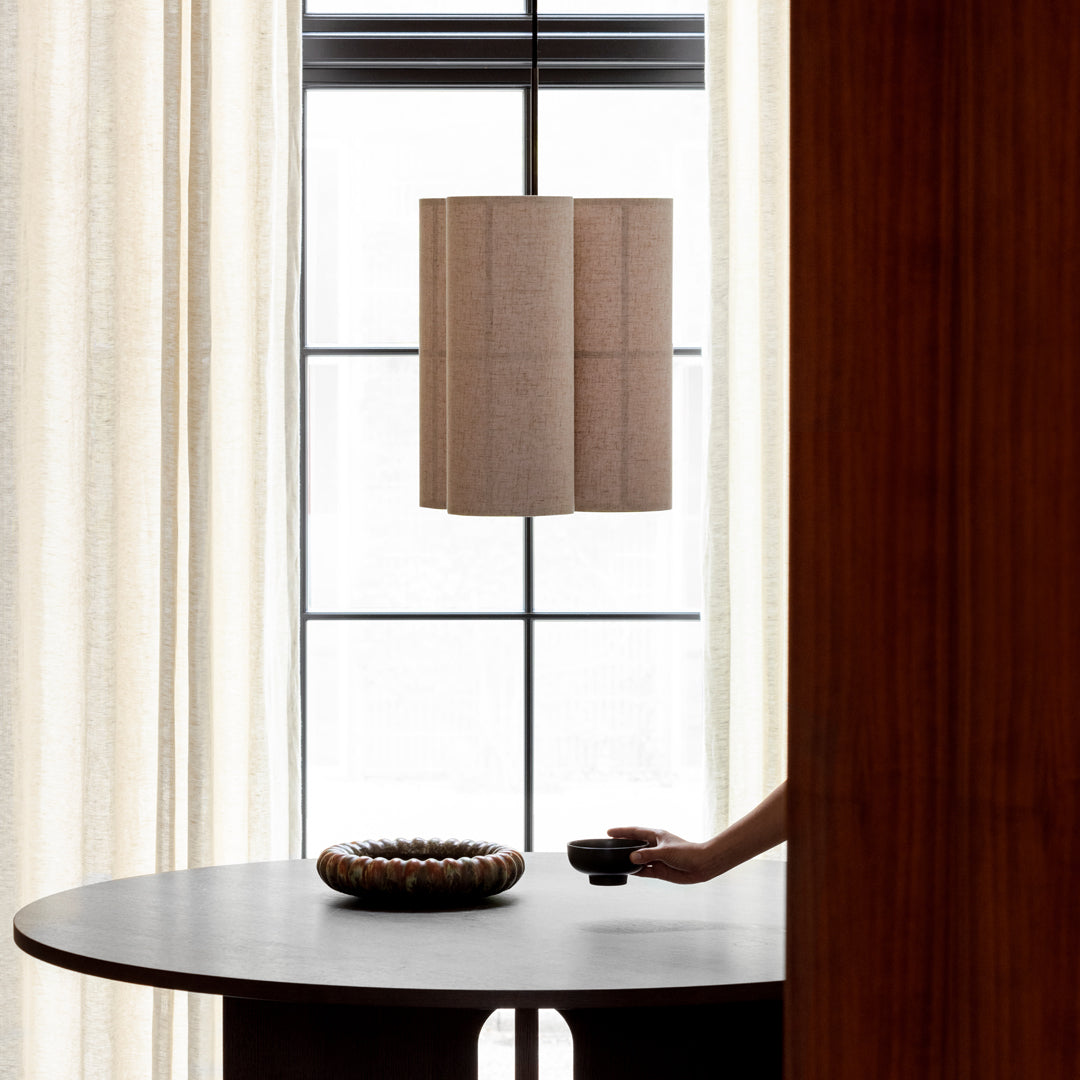Minimalist beige lamp with a textured pattern, complementing sleek dark wooden table and soft, creamy curtains.