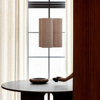 Minimalist beige lamp with a textured pattern, complementing sleek dark wooden table and soft, creamy curtains.