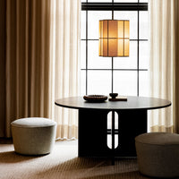 Modern round black table with light gray poufs, warm beige curtains, and geometric pendant light.