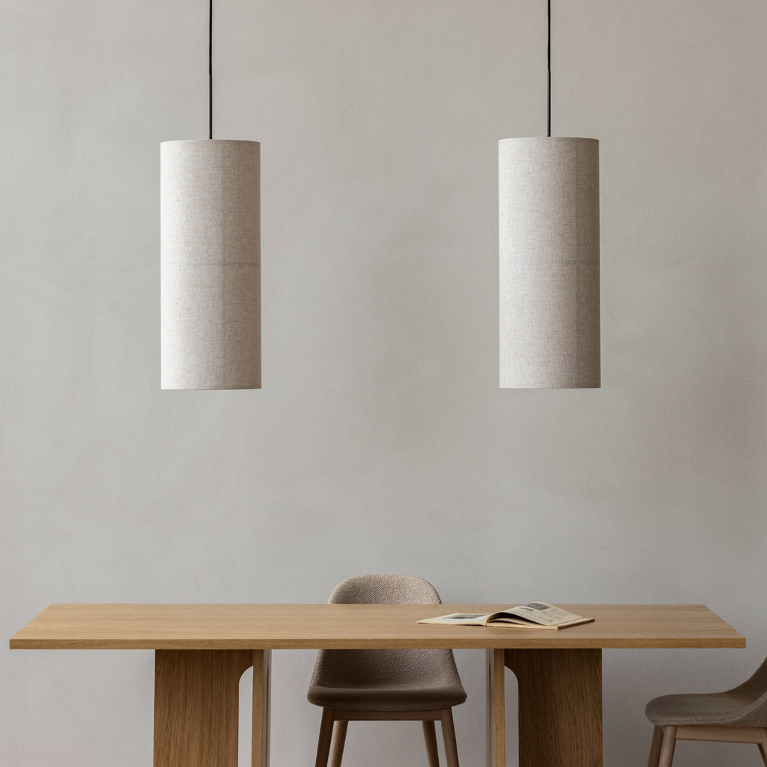 Two cylindrical pendant lights in soft beige hanging above a wooden table, creating a modern, neutral aesthetic.
