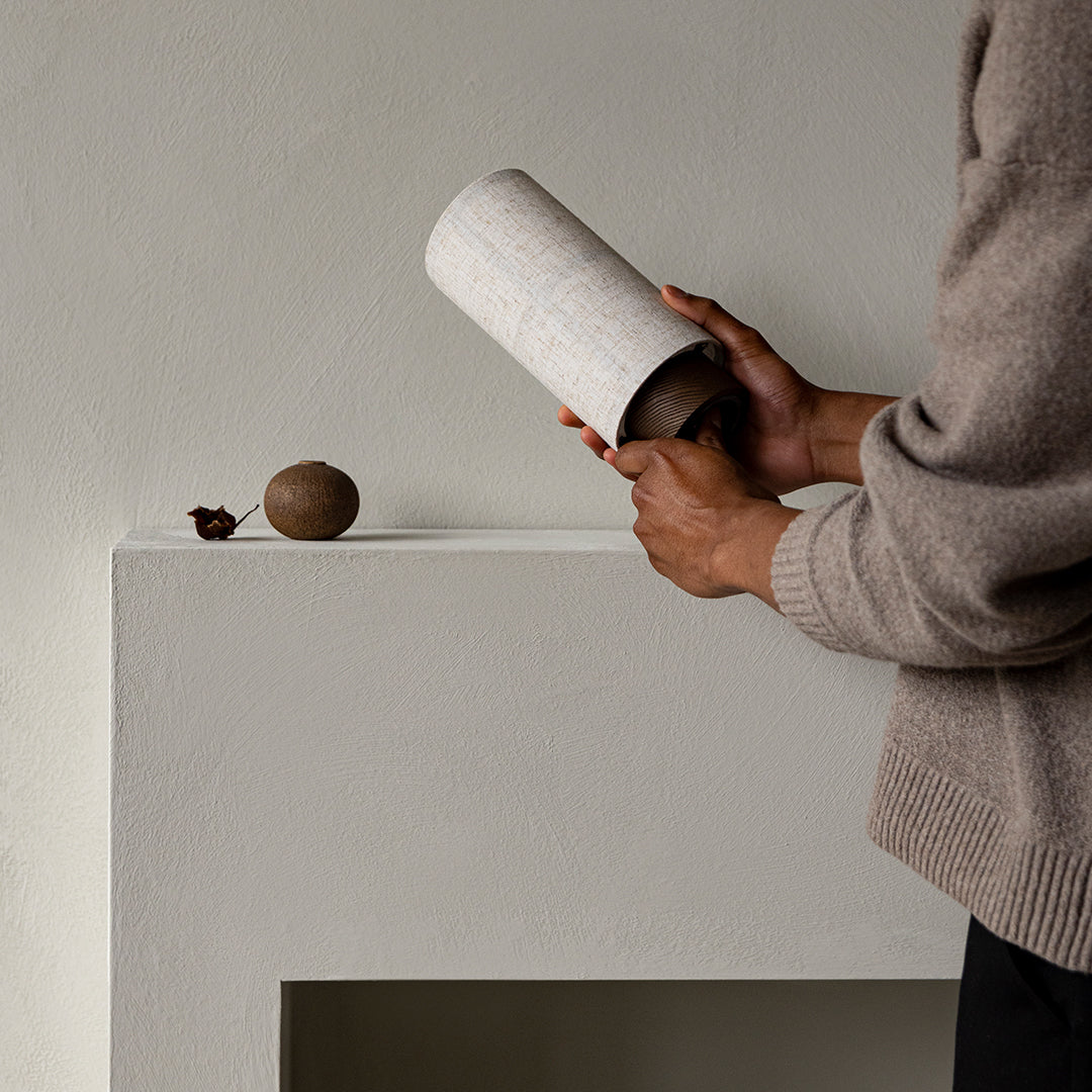 Neutral-toned ceramic vase with a textured, speckled pattern, placed on a minimalist light gray surface.