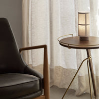 Black leather chair next to a round wooden table, featuring a soft neutral curtain backdrop and warm lighting.