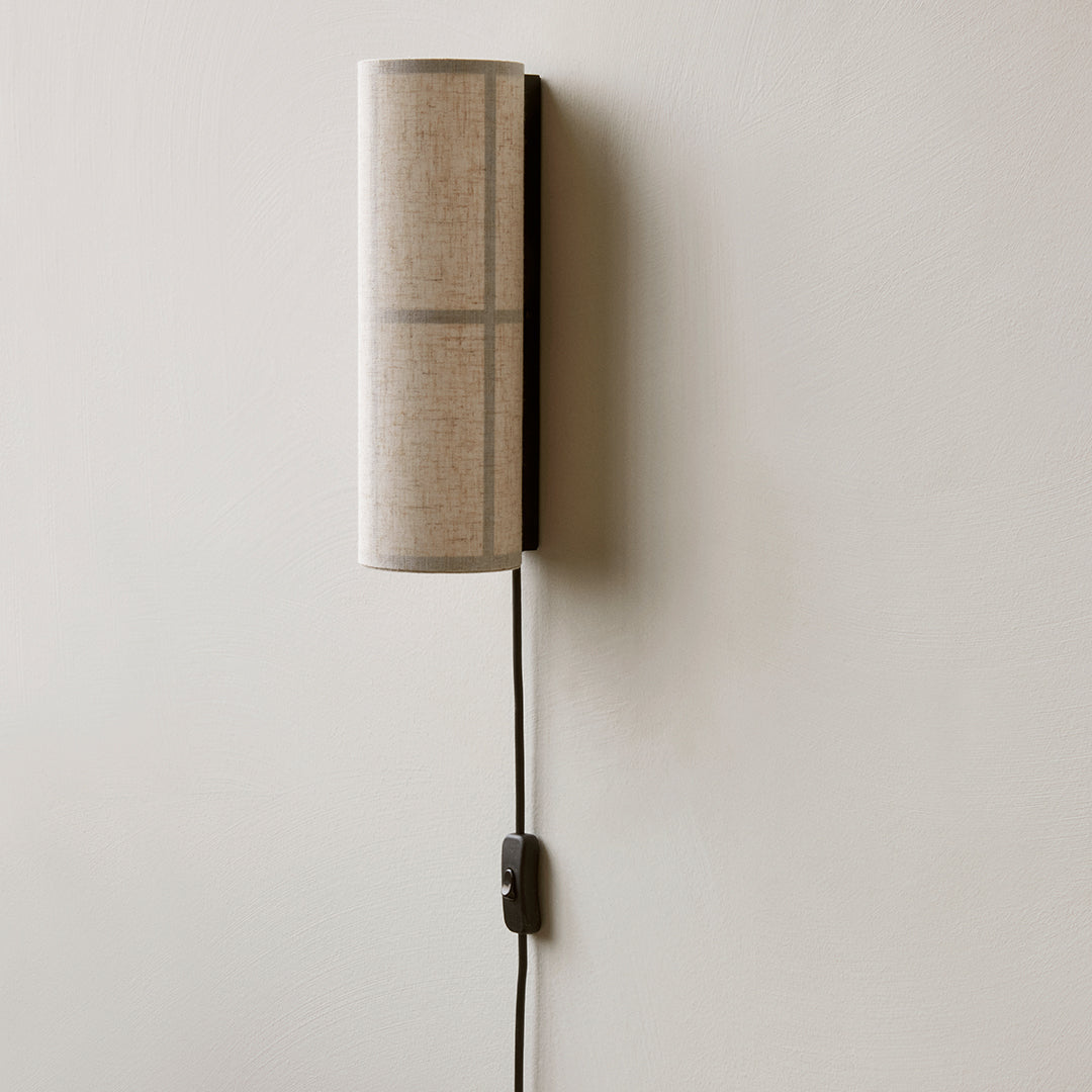 Vertical wall lamp with a beige textured pattern and black cord against a light background.