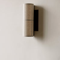 Beige cylindrical lamp shade with a subtle linen texture and a sleek black wall mount.