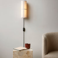 Sleek, neutral-toned wall lamp with a soft, cylindrical shade and contrasting black cord against a minimalist backdrop.