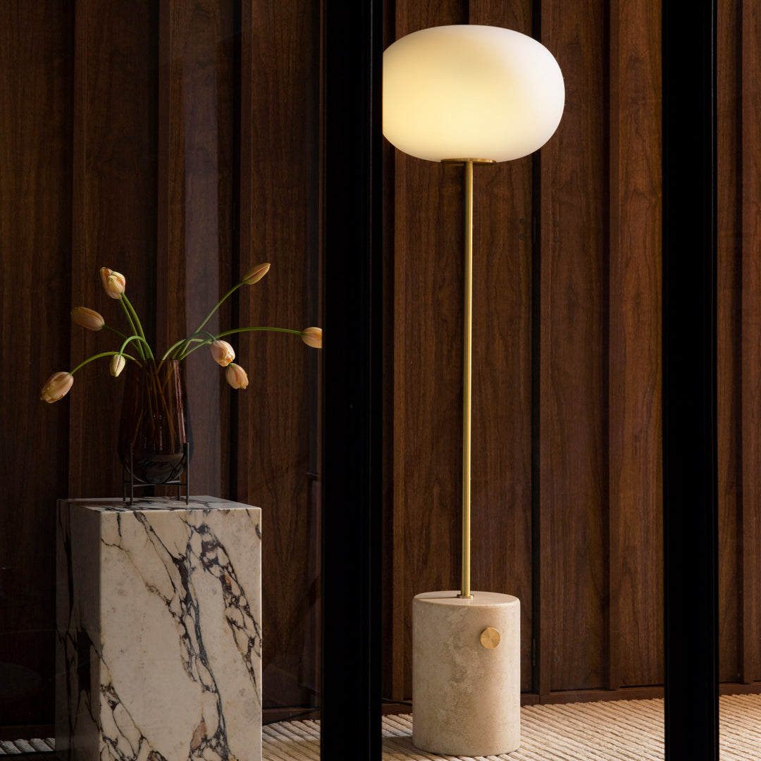 Modern white globe floor lamp on a beige marble base, set against dark wooden panels. Elegant and minimalistic design.