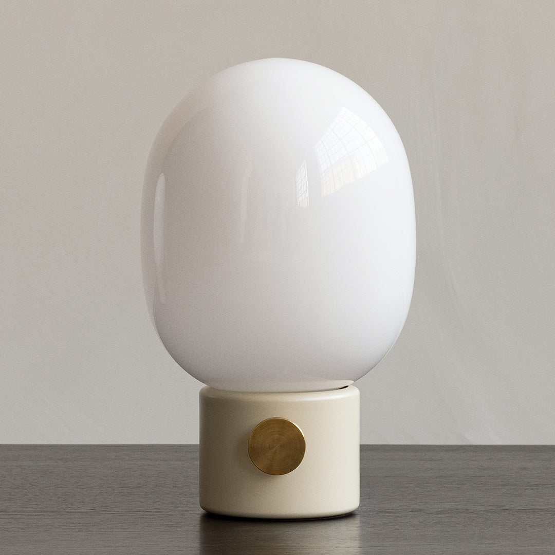 White glass lamp with a smooth, glossy finish and a minimalist beige base featuring a circular accent.