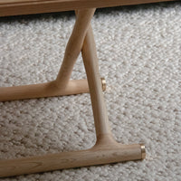 Light natural wood with smooth finish, featuring sleek lines and subtle metallic accents, set against a textured beige carpet.