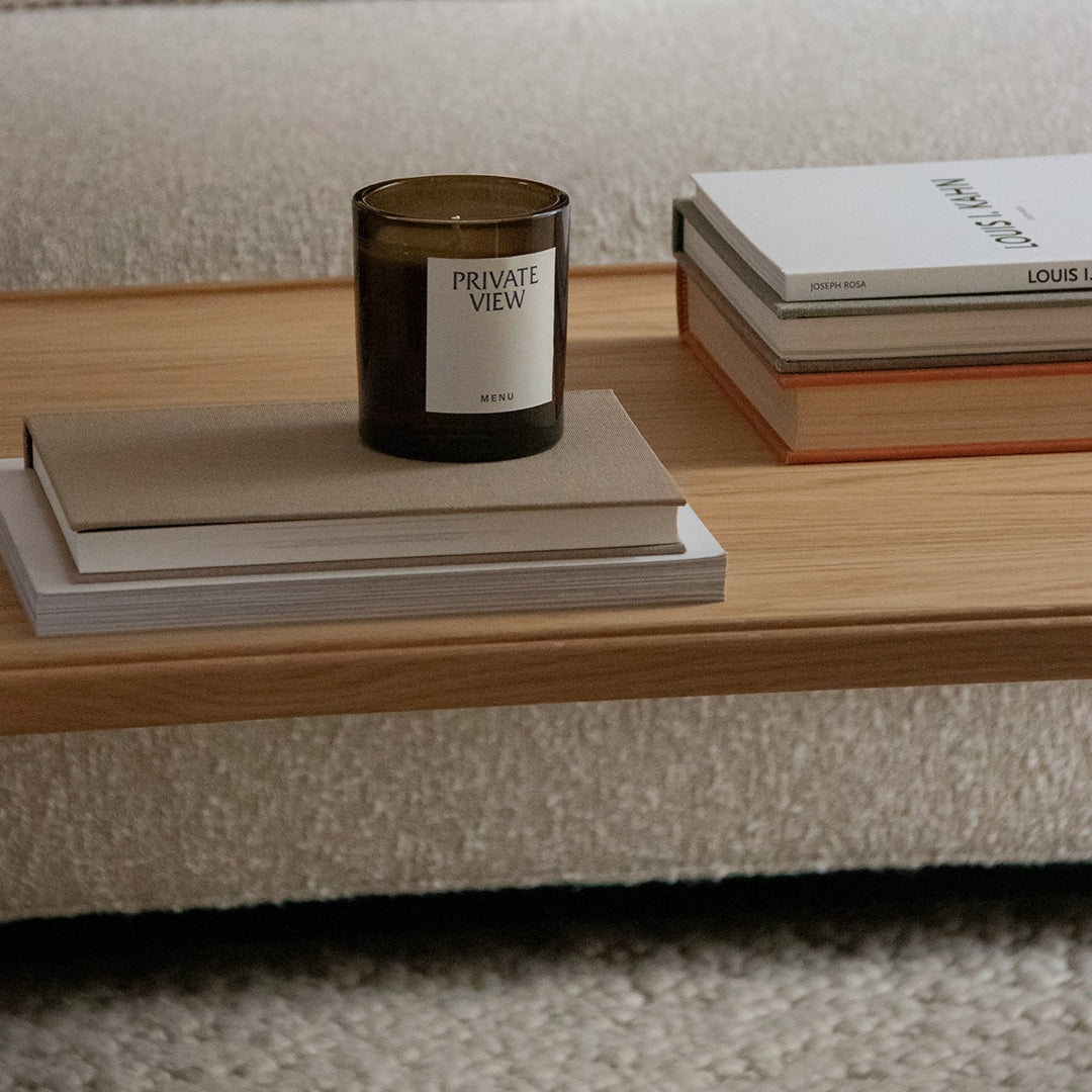 Wooden table with books in neutral tones and a dark candle, set against a textured, light-colored background.