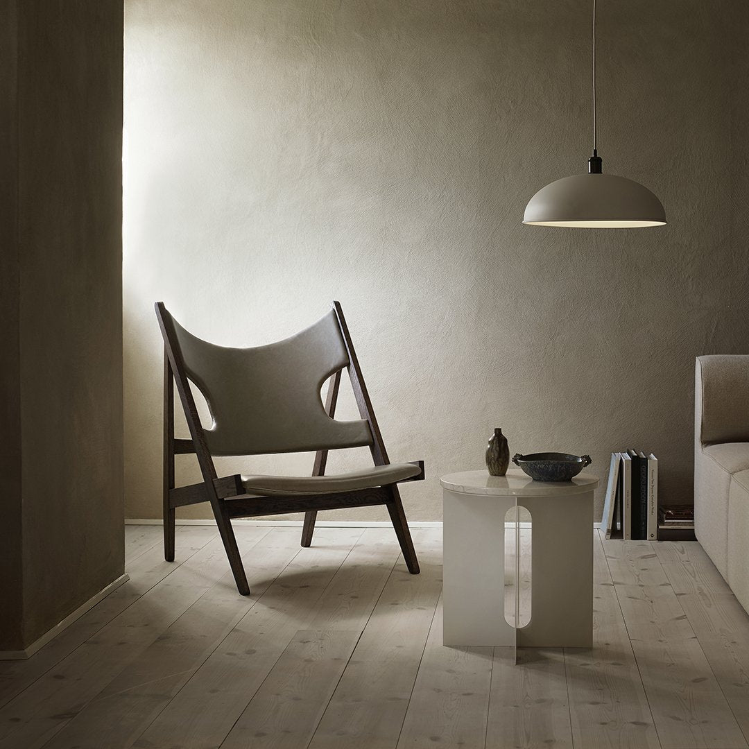 "Neutral beige walls with a soft gray chair, white table, and simple black lamp create a serene modern aesthetic."