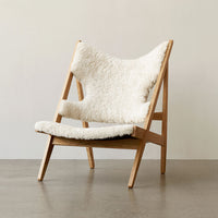 Cozy white shearling chair with natural wood frame, featuring a minimalist design and soft texture.