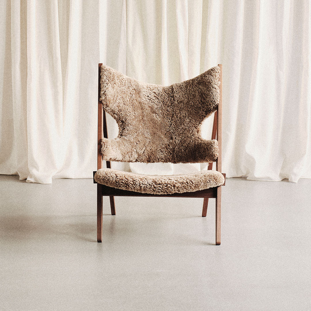 Brown upholstered chair with a unique textured pattern, set against a light, neutral curtain backdrop.