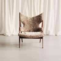 Brown upholstered chair with a unique textured pattern, set against a light, neutral curtain backdrop.