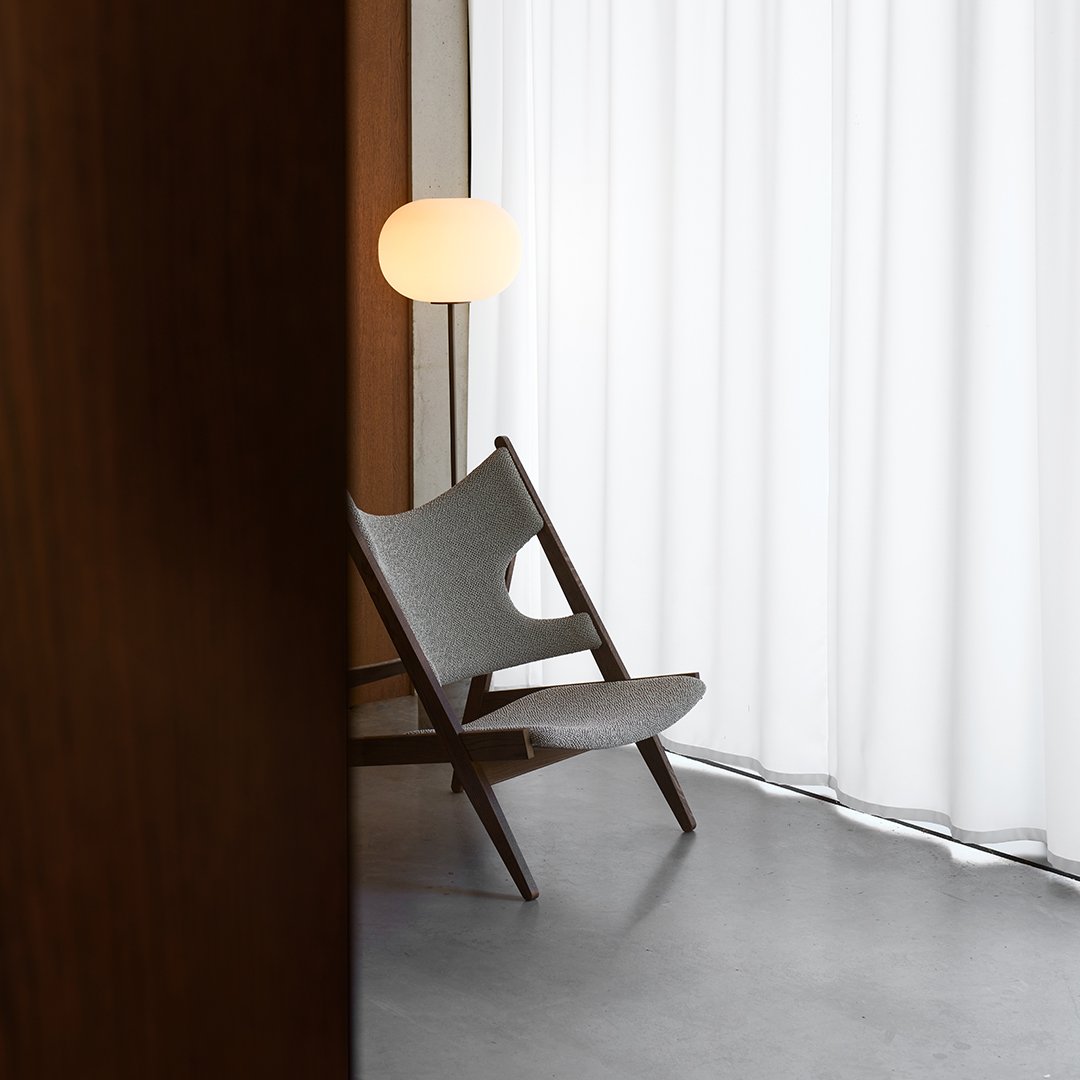 Gray-patterned chair against a backdrop of white curtains and warm wood tones, showcasing minimalist design aesthetics.
