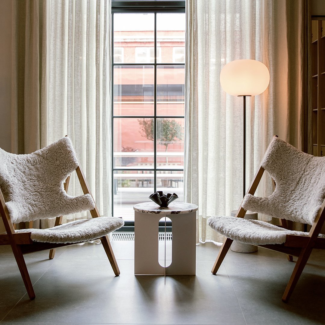 Neutral-toned chairs with textured white upholstery, natural wood frames, and a minimalist white side table.