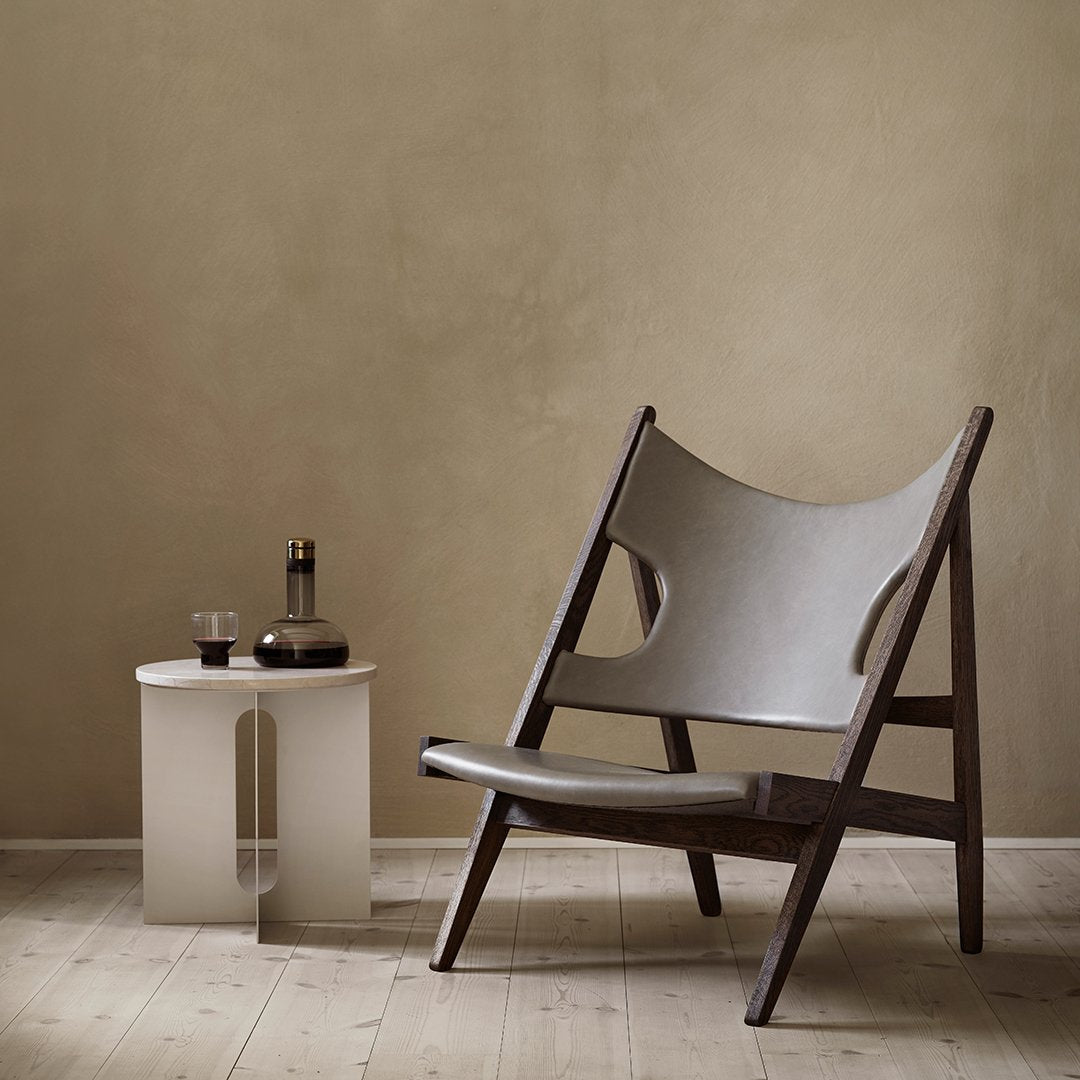 Stylish gray fabric lounge chair with dark wood frame, minimalist design against a warm beige wall.