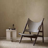 Stylish gray fabric lounge chair with dark wood frame, minimalist design against a warm beige wall.
