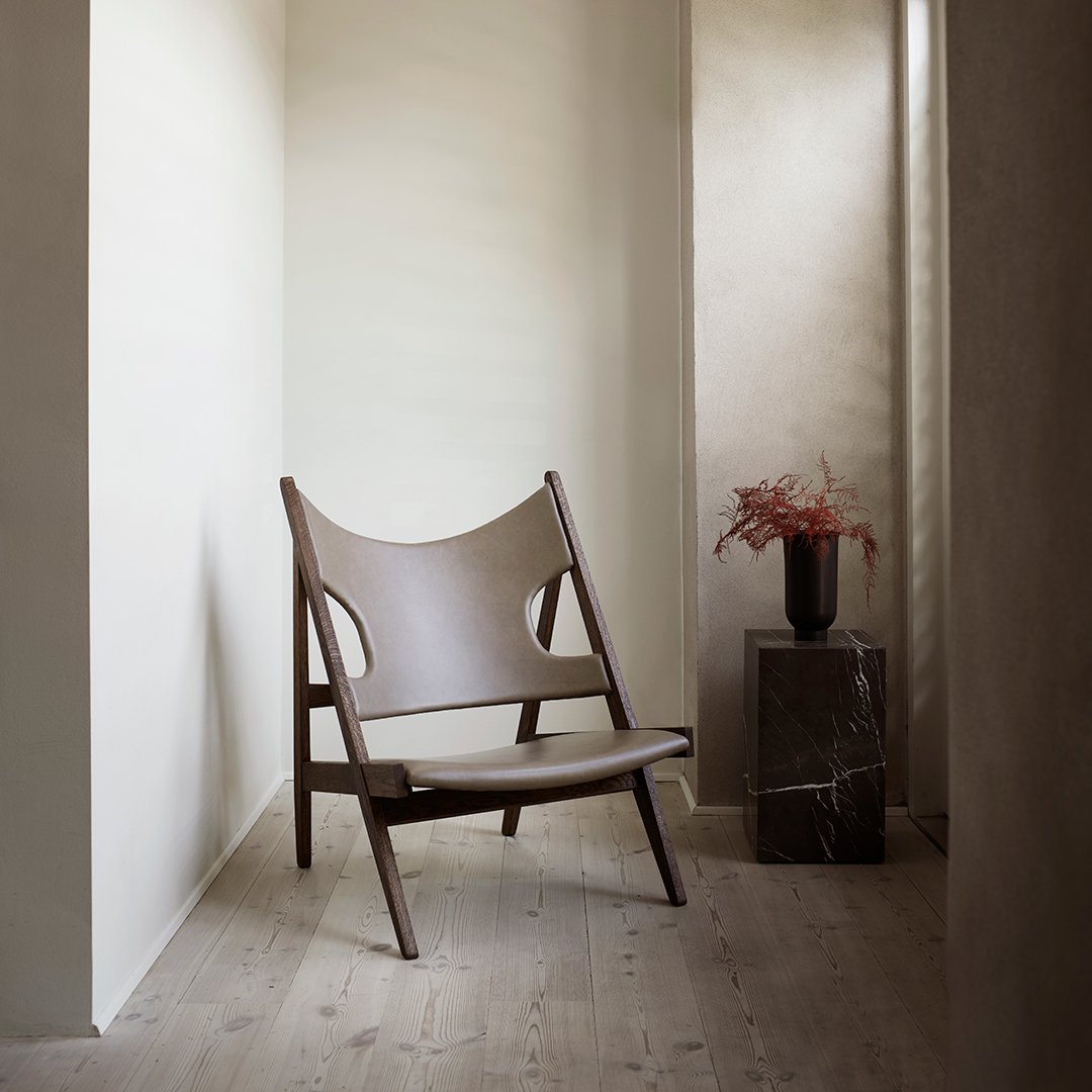 Brown leather chair with a minimalist design, featuring a smooth finish and natural wood accents in a neutral-toned interior.