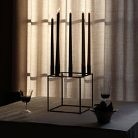 "Elegant black and brown taper candles on a modern geometric holder with soft beige curtains as backdrop."