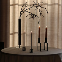 Stylish black candle holders with white and amber candles on a neutral table against a soft, light-filtering backdrop.