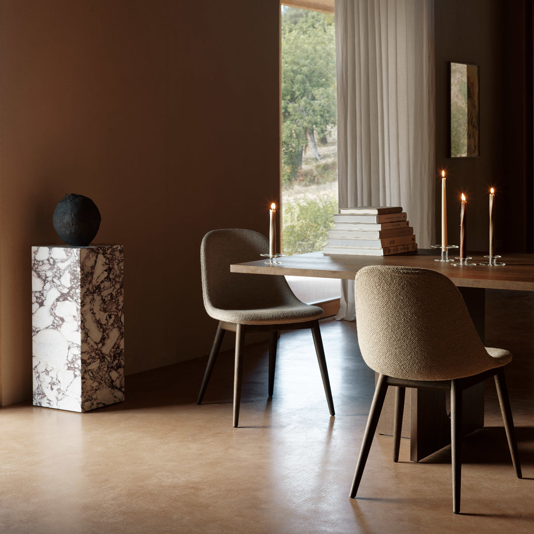 Beige chairs and a marble pedestal with striking black and white veining in a warm, earthy-toned dining space.