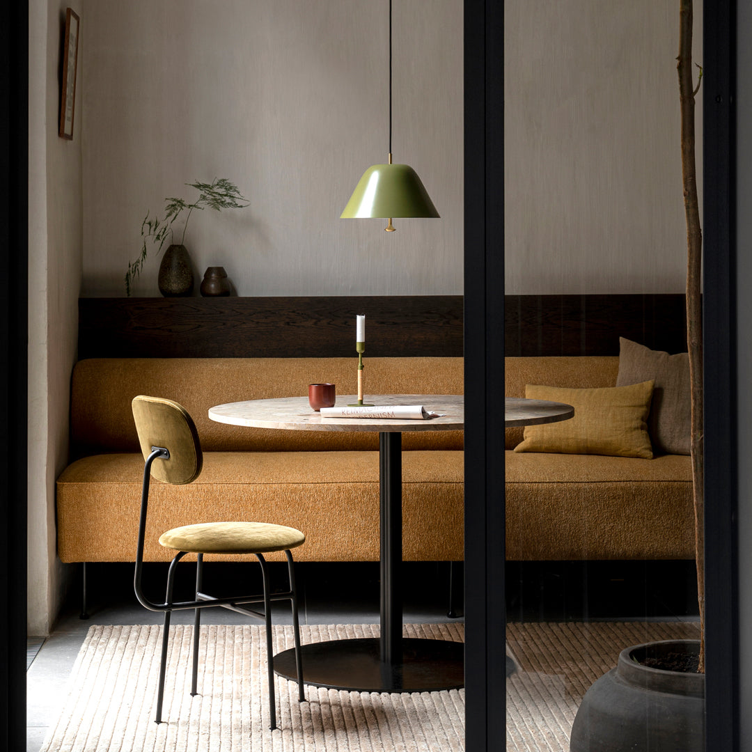 Modern dining area with warm brown tones, green lamp, and textured textiles in a minimalistic design.