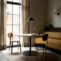 Scandinavian-style dining area featuring earthy tones, mustard yellow upholstery, green lamp, and neutral curtains.