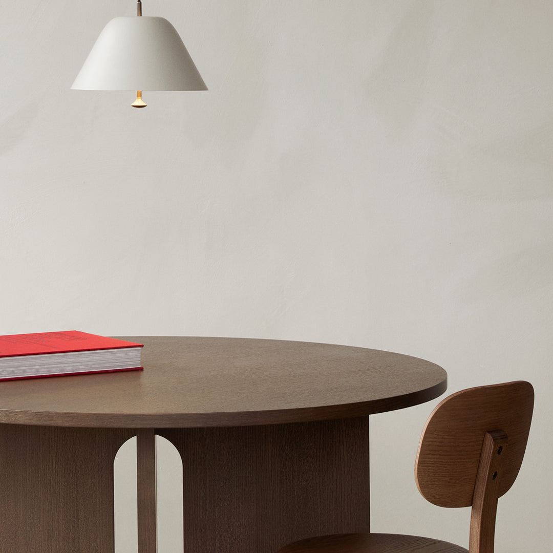 Round brown wooden table with a white pendant lamp and red book, featuring a minimalist, contemporary design.
