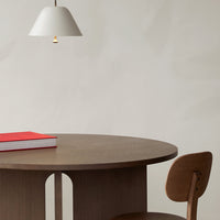 Round brown wooden table with a white pendant lamp and red book, featuring a minimalist, contemporary design.