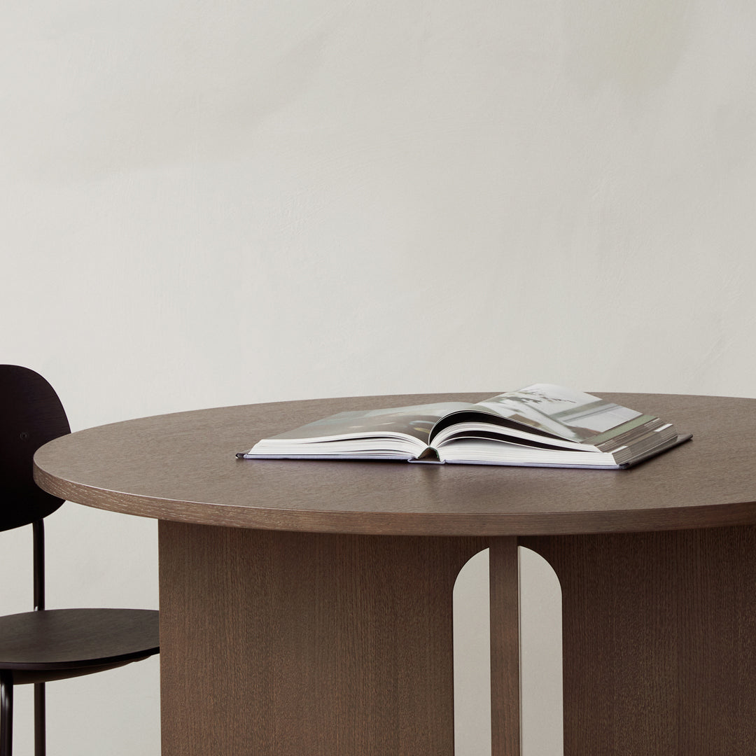 "Round brown wooden table with clean lines, featuring a minimalist design and a sleek black chair."