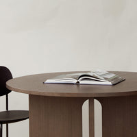 "Round brown wooden table with clean lines, featuring a minimalist design and a sleek black chair."